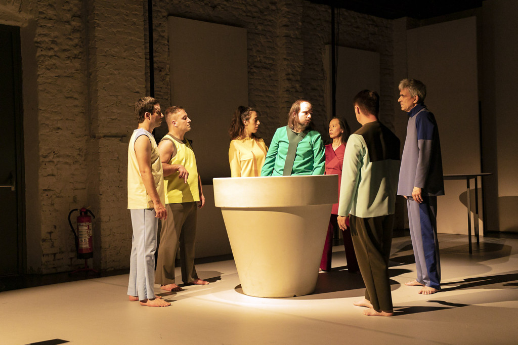 Scene photo of a performance: A couple people stand around a flower pot. one is in the flower pot.