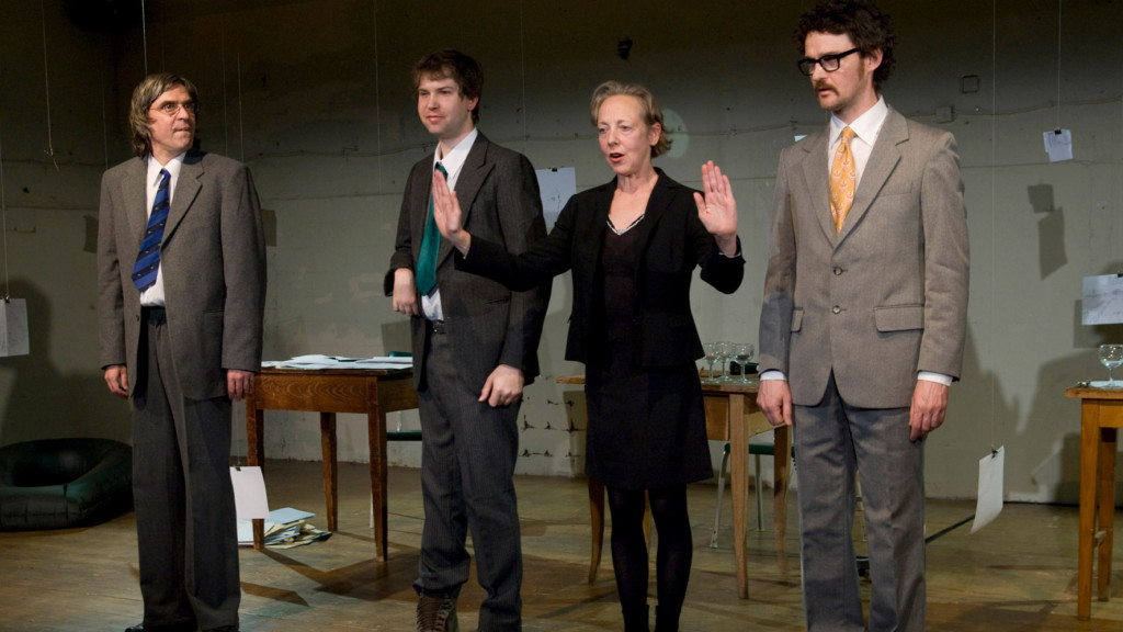 Szenenfoto aus einer Auffuehrung: Vier Personen stehen auf einer Theaterbuehne nebeneinander.