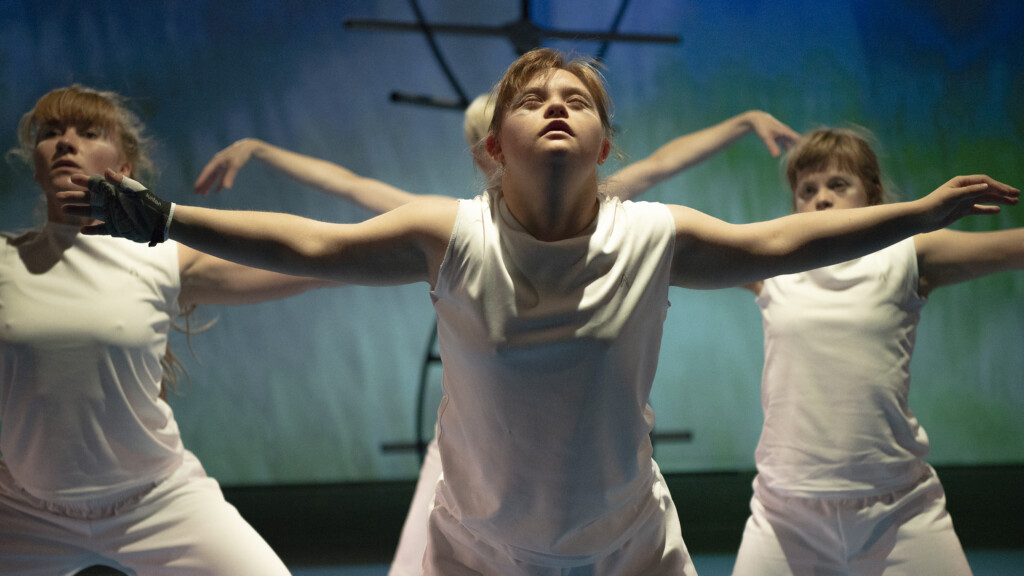 Scene photo of a performance: A couple of people in front of a and on a DNA object on a stage.