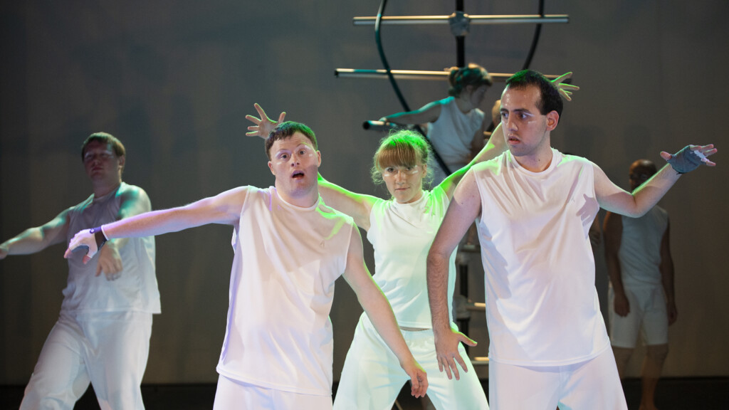 Scene photo of a performance: Four people on a stage. A DNA objects is in the background.