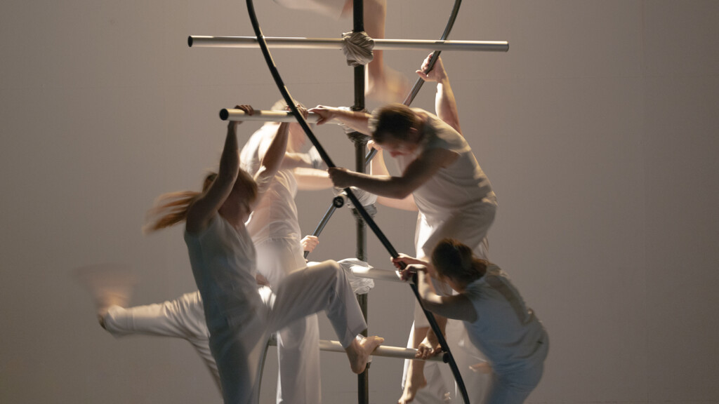 Scene photo of a performance: Four people on a DNA object an a stage.