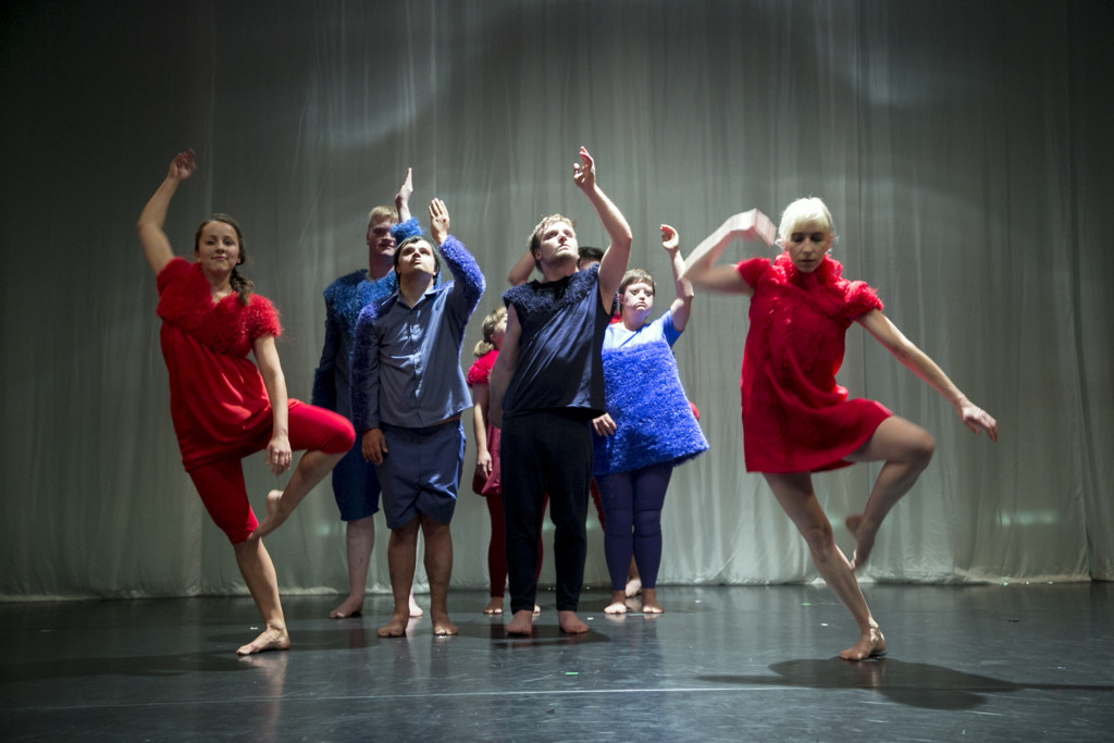 Szenen-Foto aus einer Aufführung: Mehrere Personen tanzen und stehen auf einer Bühne.