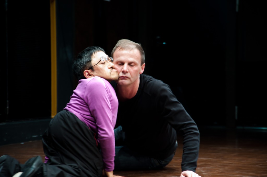 Scene photo of a performance: Two men are sitting on the ground with closed eyes.