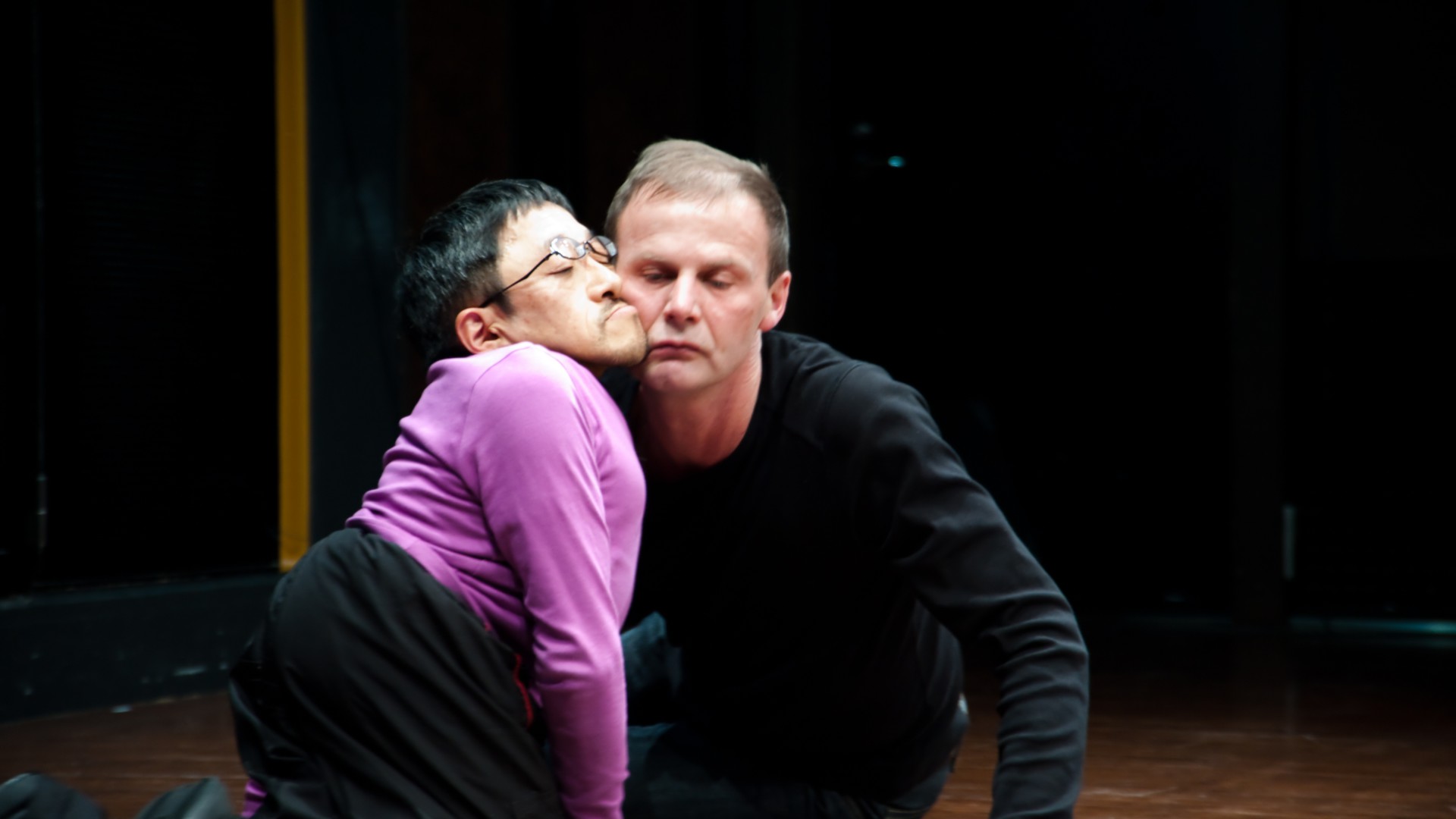 Scene photo of a performance: Two men are sitting on the ground with closed eyes.