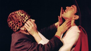 Szenenfoto aus einer Auffuehrung: Eine Frau mit Tigerfellkappe und ein Mann berühren gegenseitig ihre Gesichter.n