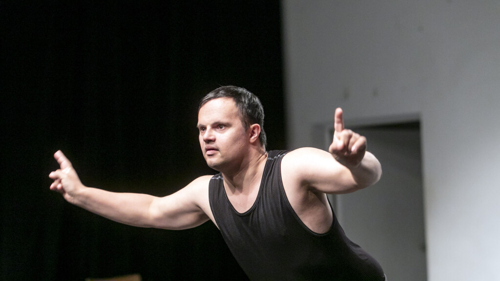 Scene photo of a performance:a man with wide-open arms on a stage.
