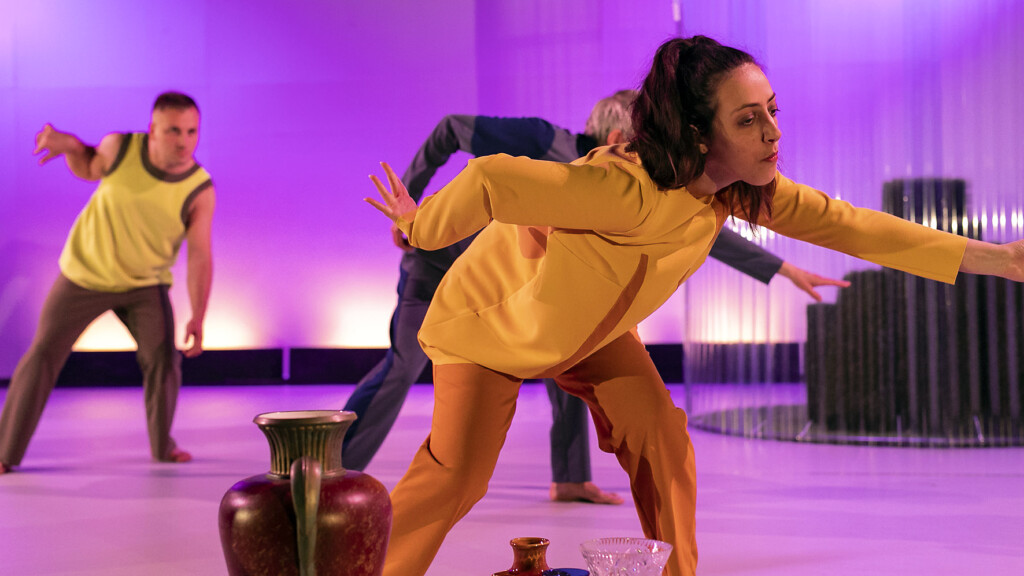 Scene photo of a performance: Three people dancing on a stage. Vases in front of them.