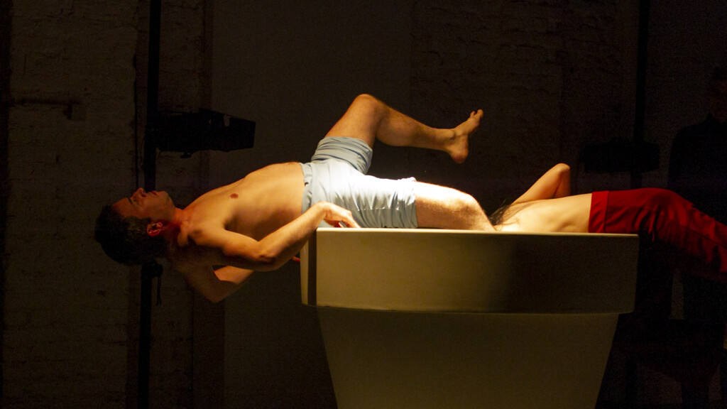 Scene photo of a performance: Two people lie on a big flower pot.