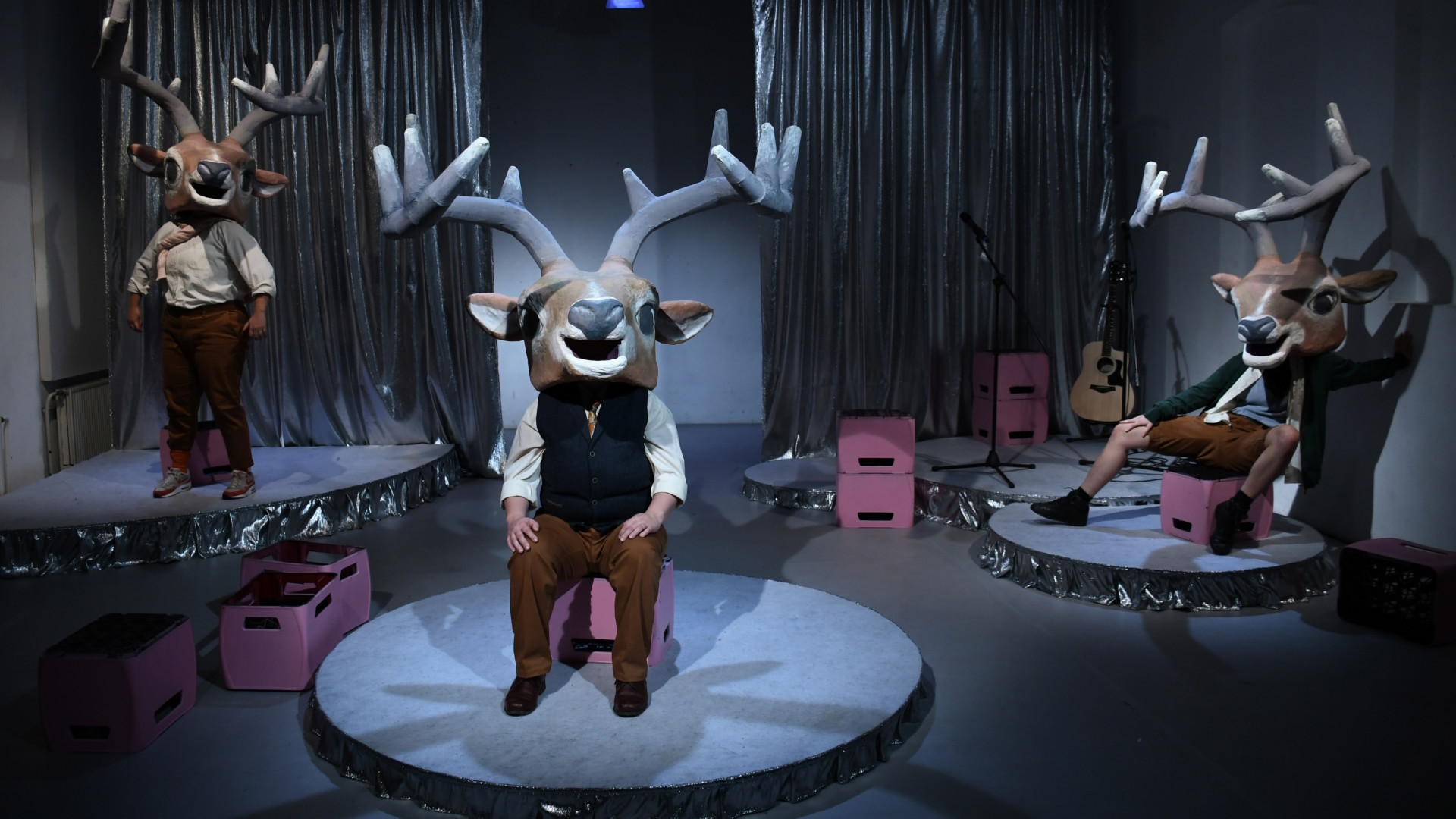 Scene photo of a performance: three actors wear deer masks with antlers and are on separate bases.