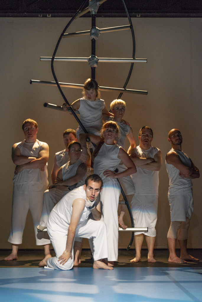 Scene photo of a performance: A couple of people in front of a and on a DNA object on a stage.