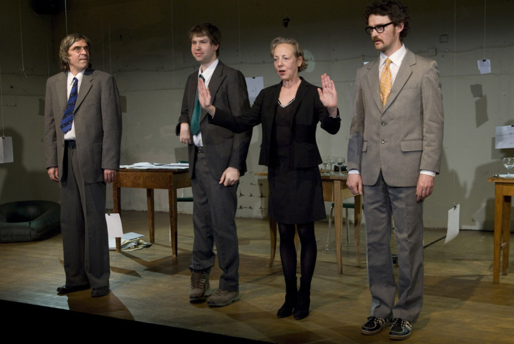 Szenenfoto aus einer Auffuehrung: Vier Personen stehen auf einer Theaterbuehne nebeneinander.