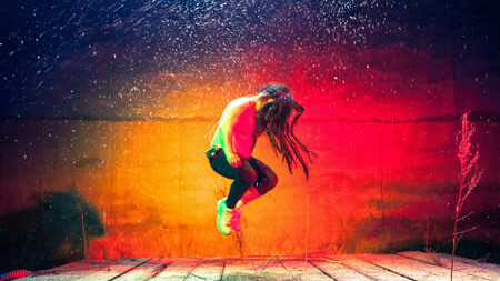 Scene photo of a performance: Colorful background. One person is jumping on a stage.