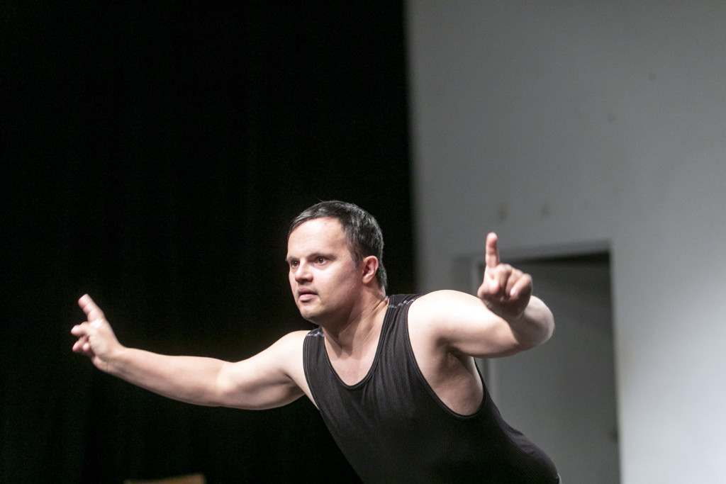 Scene photo of a performance:a man with wide-open arms on a stage.