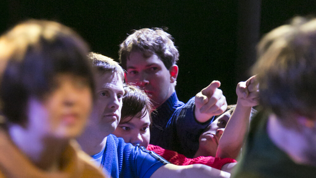 Szenenfoto aus einer Aufführung: Mehrere Menschen in Großaufnahme. Alle zeigen mit den Fingern in eine Richtung