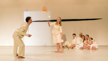 Scene photo of a performance: A young man to the left and other people on the right on a stage.