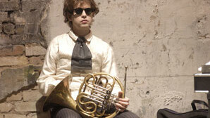 A man wearing sunglasses sitting on a chair holding a French horn.