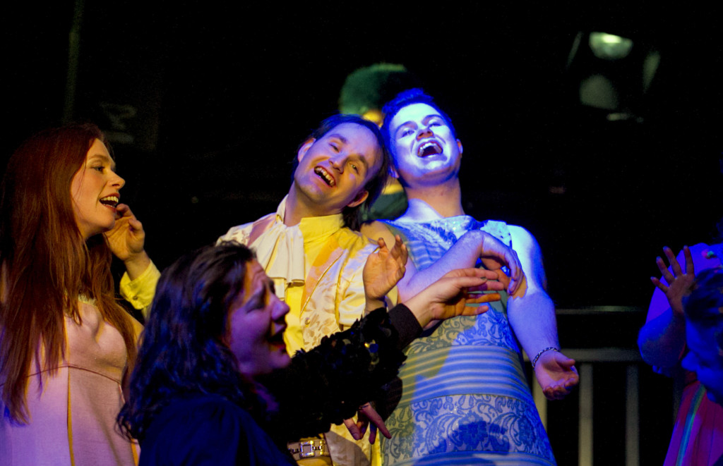 Szenenfoto aus einer Auffuehrung: Vier Personen lachend auf einer Theaterbuehne.