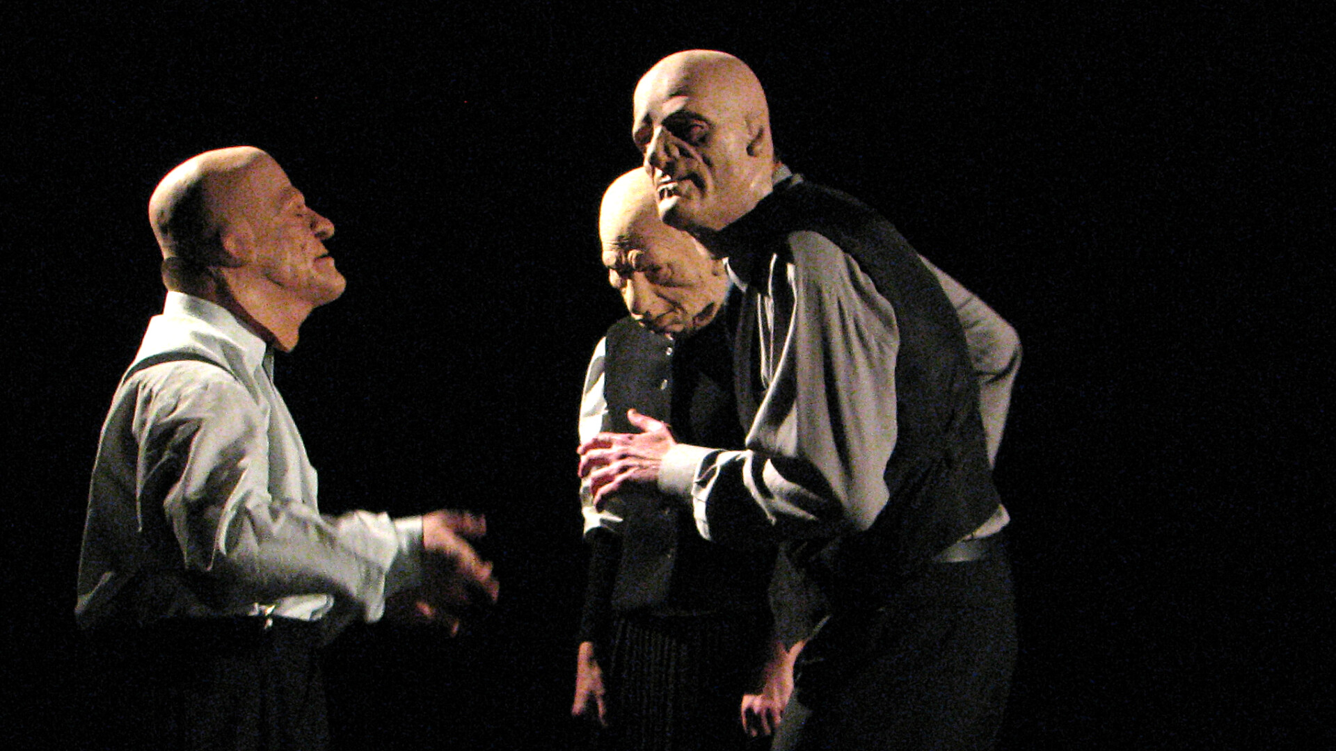 3 men wearing rubbermasks are standing in a circle.