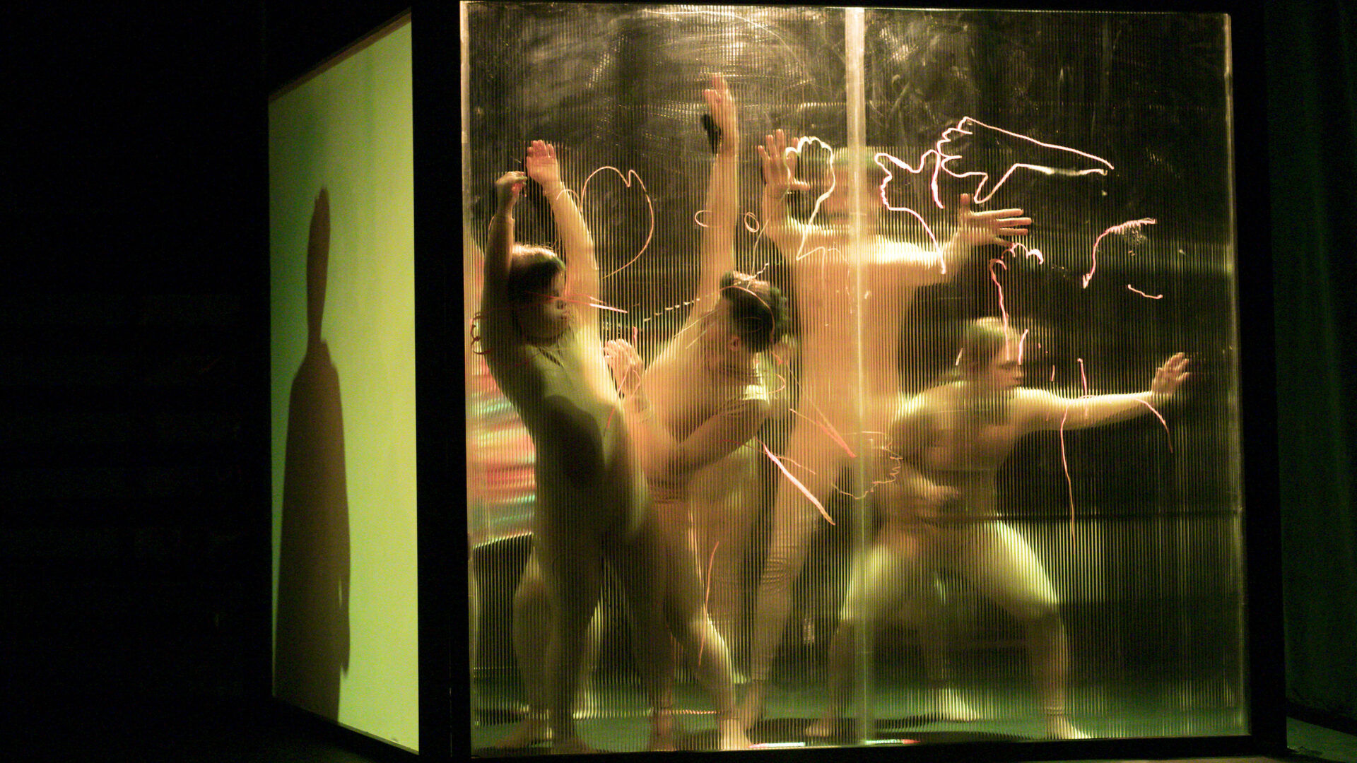scene photo of a performance: four people behind a transparent wall.