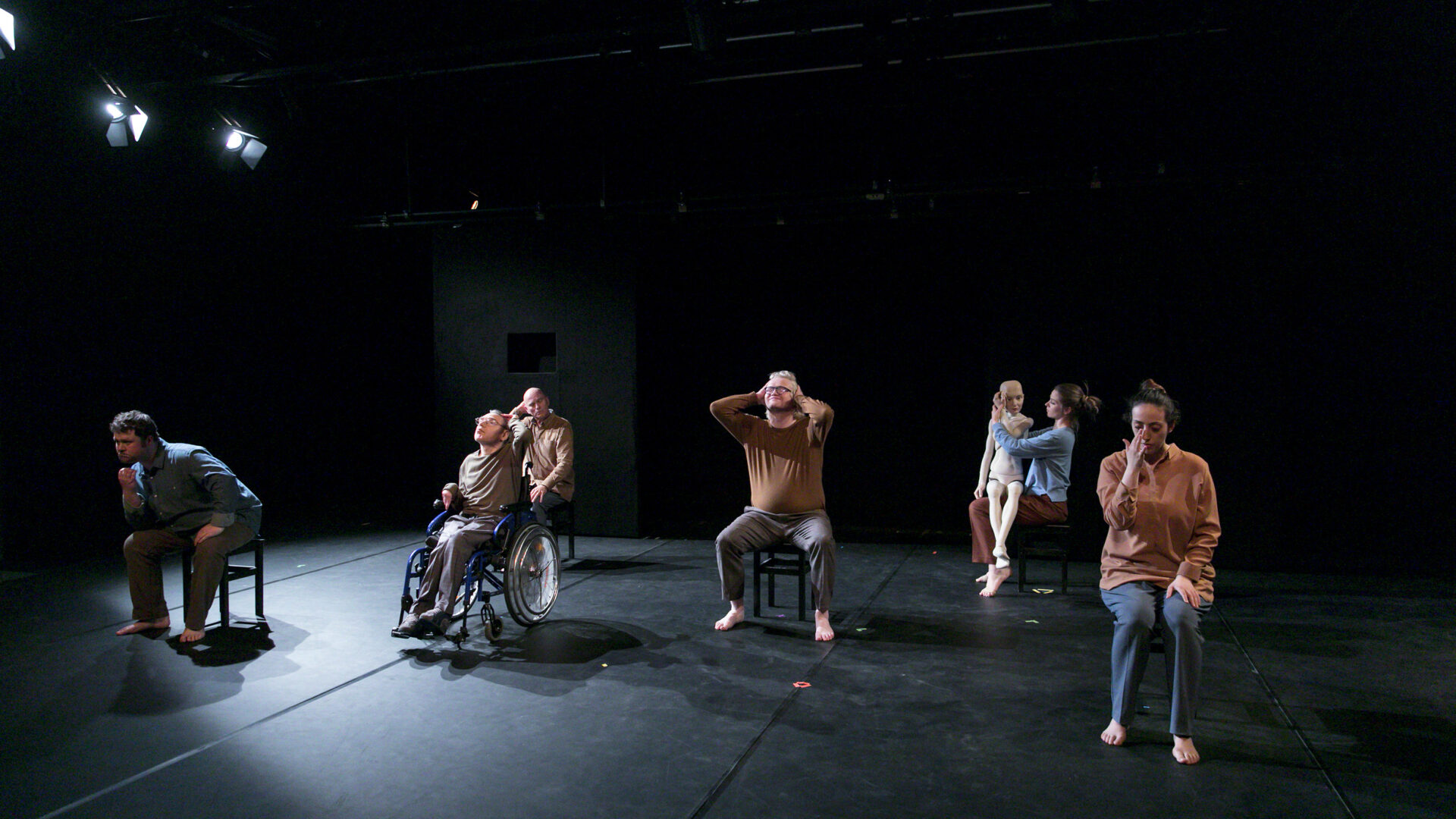 Scene photo of a performance: A couple people are sitting on small chairs on a stage.