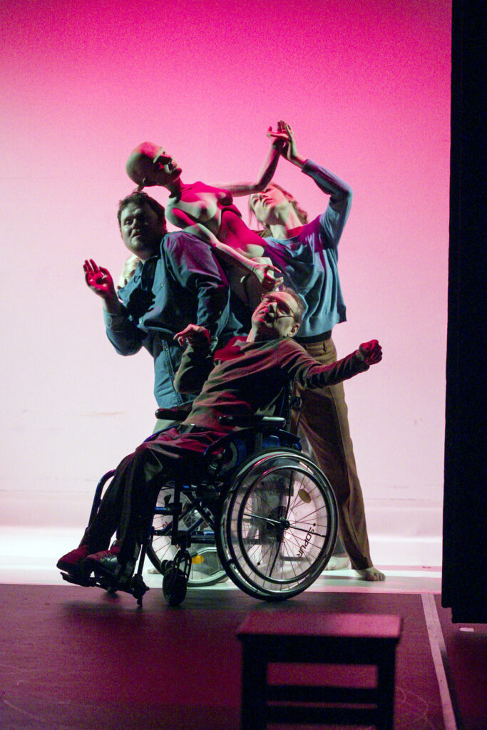 Scene photo of a performance: Three people are moving on a stage. One puppet in the middle.