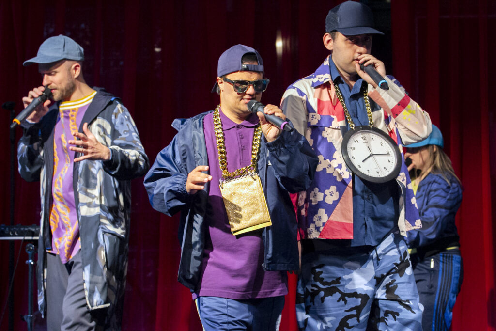 Scene photo of a performance: A couple people on a stage. They look like hip hop artists.