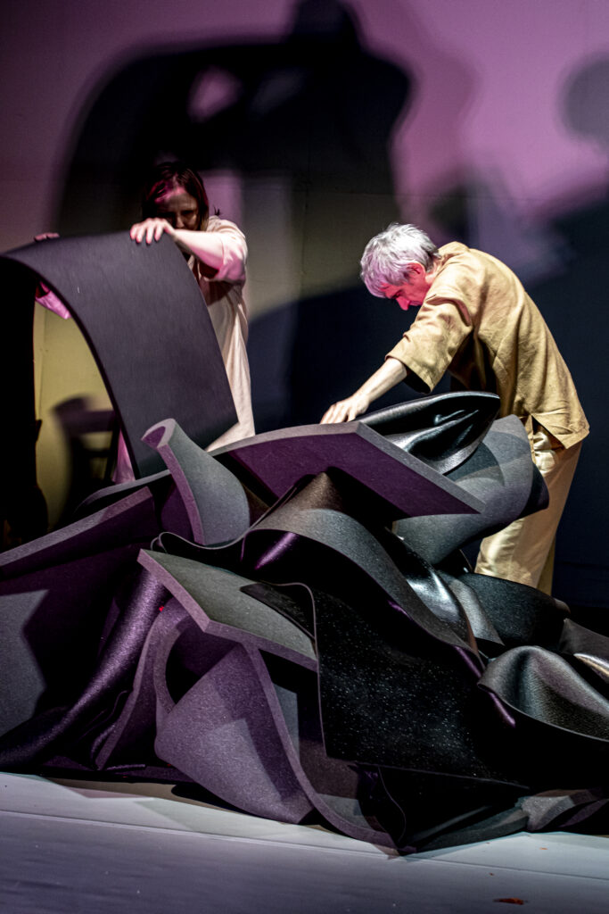 Scene photo of a performance: A pile of mats. A person is lifting up a mat.