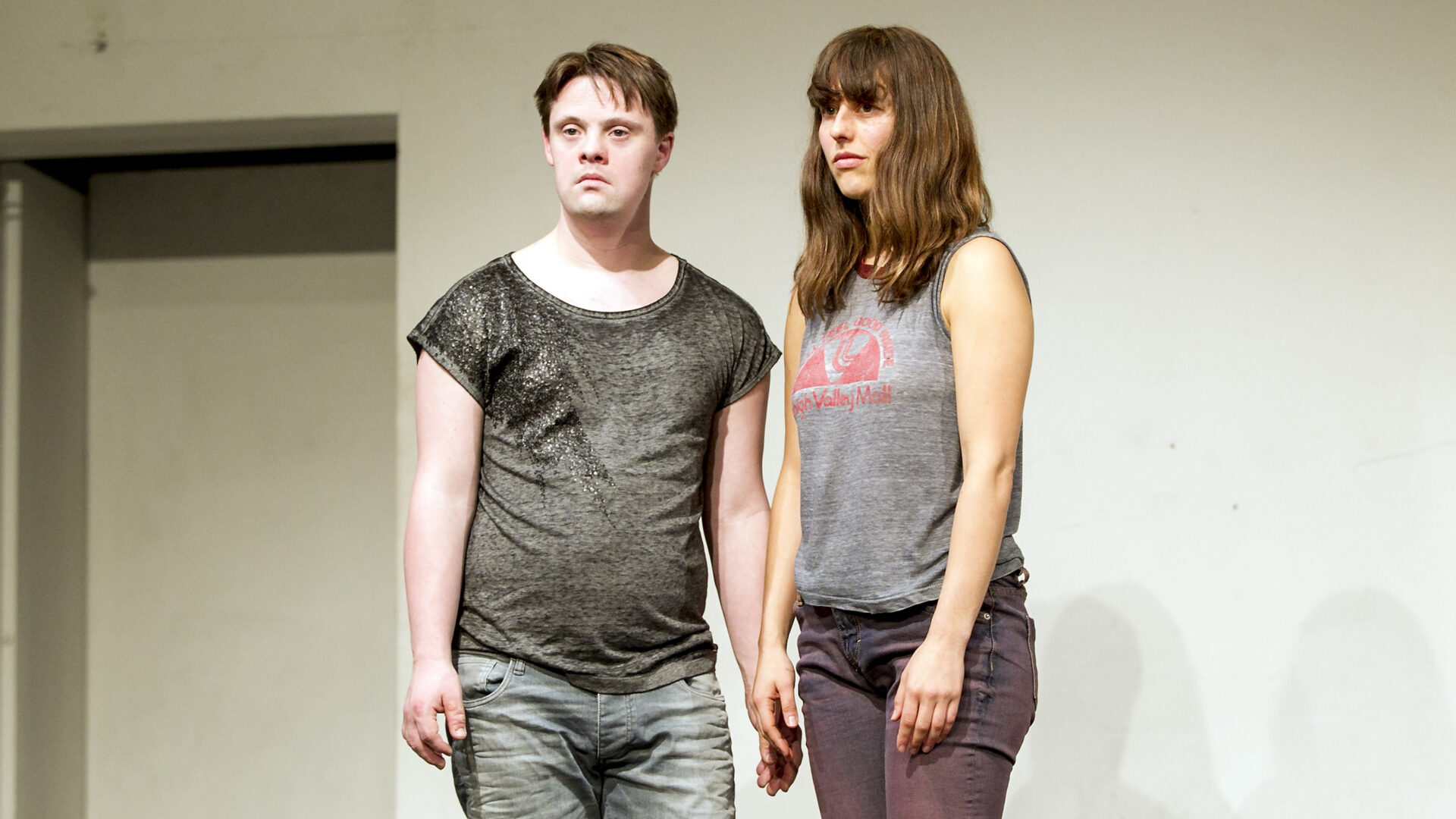 Scene photo of a performance: a man and a woman next to eachother on the stage. They are looking in the direction of the audience.