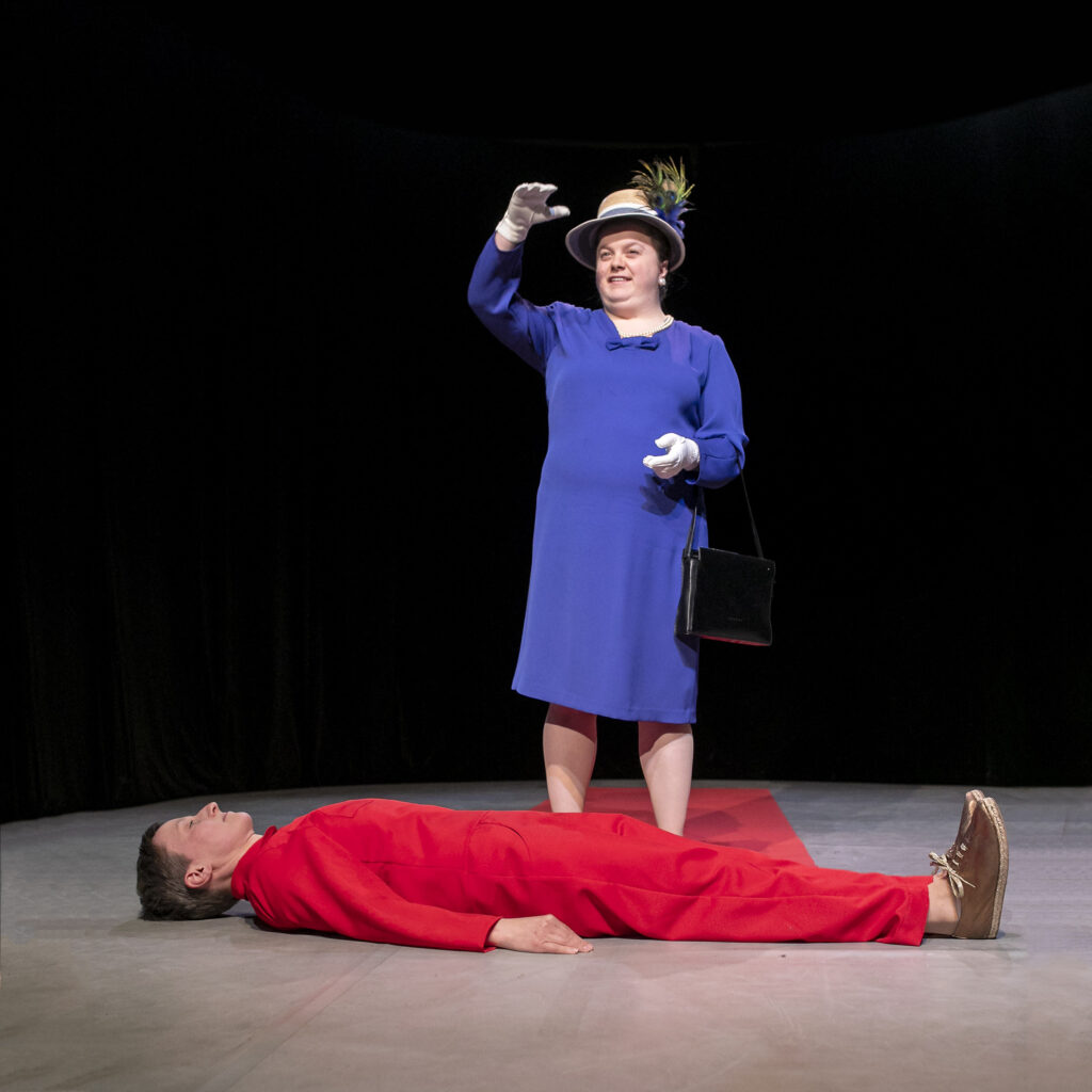 Scene photo of a performance: One person is lying on the ground. The other one is standing behind her.