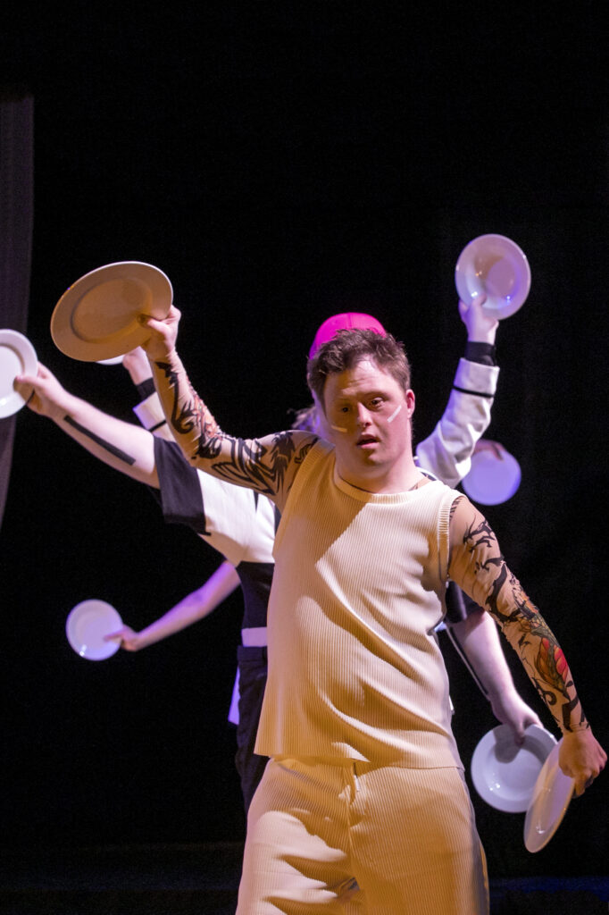 Scene Photo of a performance A person with Plates in their hands. Arms from other people behind him with plates.