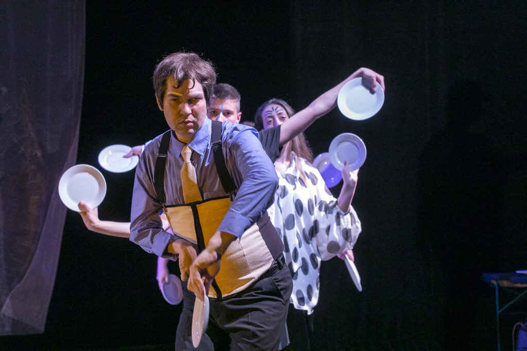 Scene photo of a performance: A couple people behind each other. The hold plates in their hands.