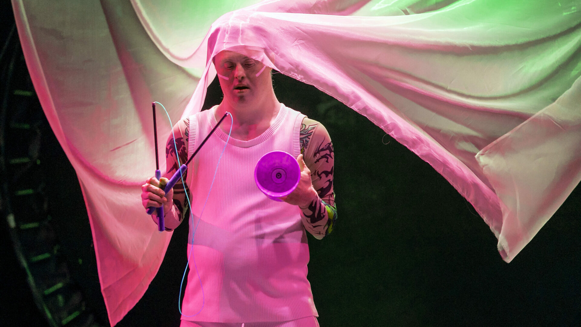 Scene photo of a performance: A person with a diabolo steps out of a white curtain on the stage.