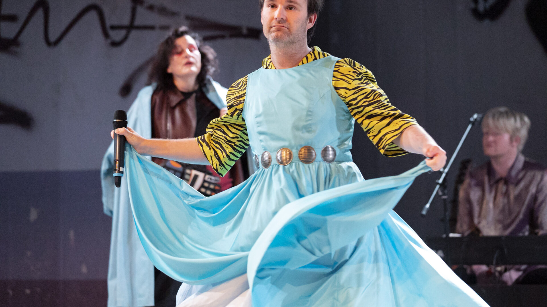 Scene photo of a performance: One man with a bright blue dress on a stage